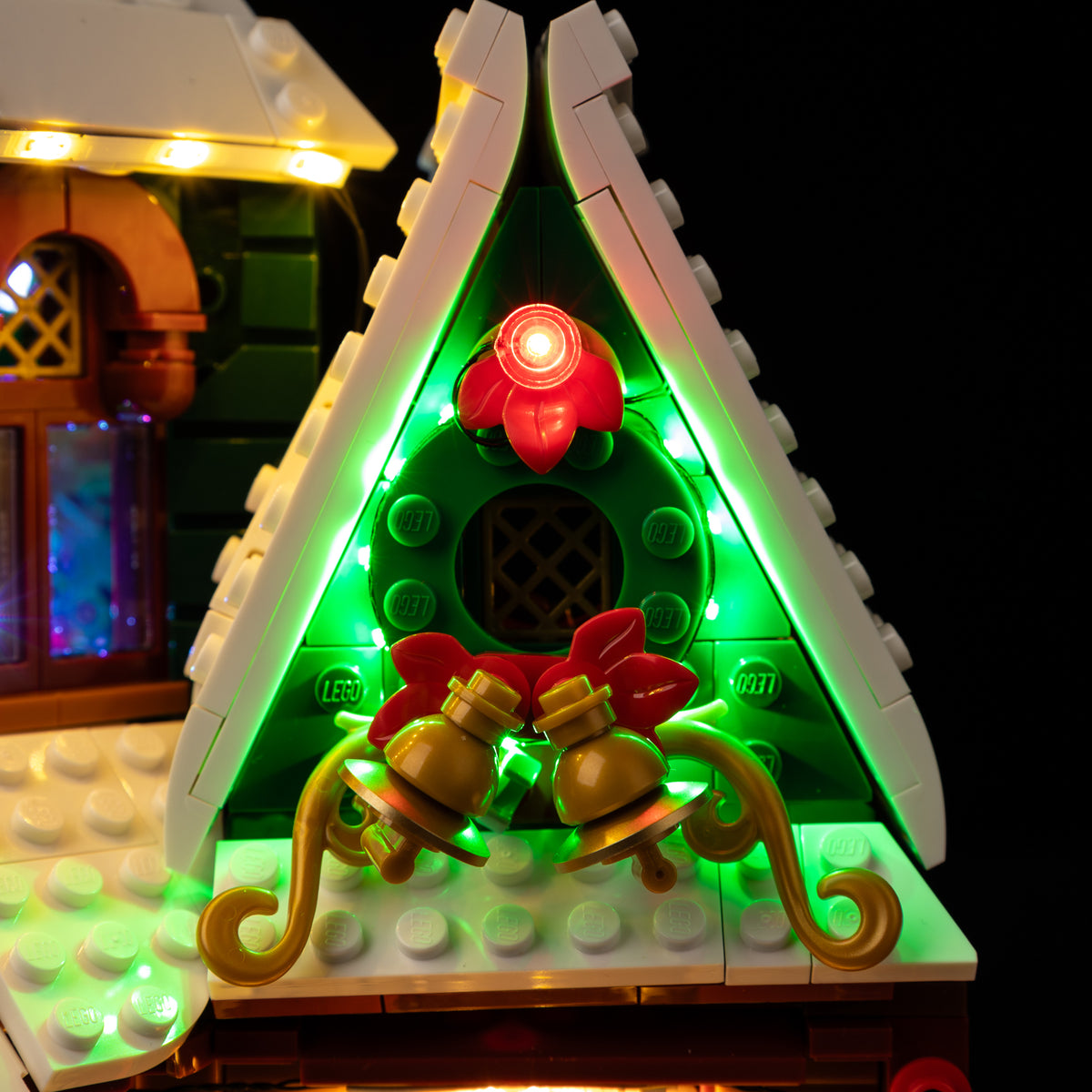 Green kit lighting around the snowy gable, holly decoration and golden bells on LEGO Holiday House.