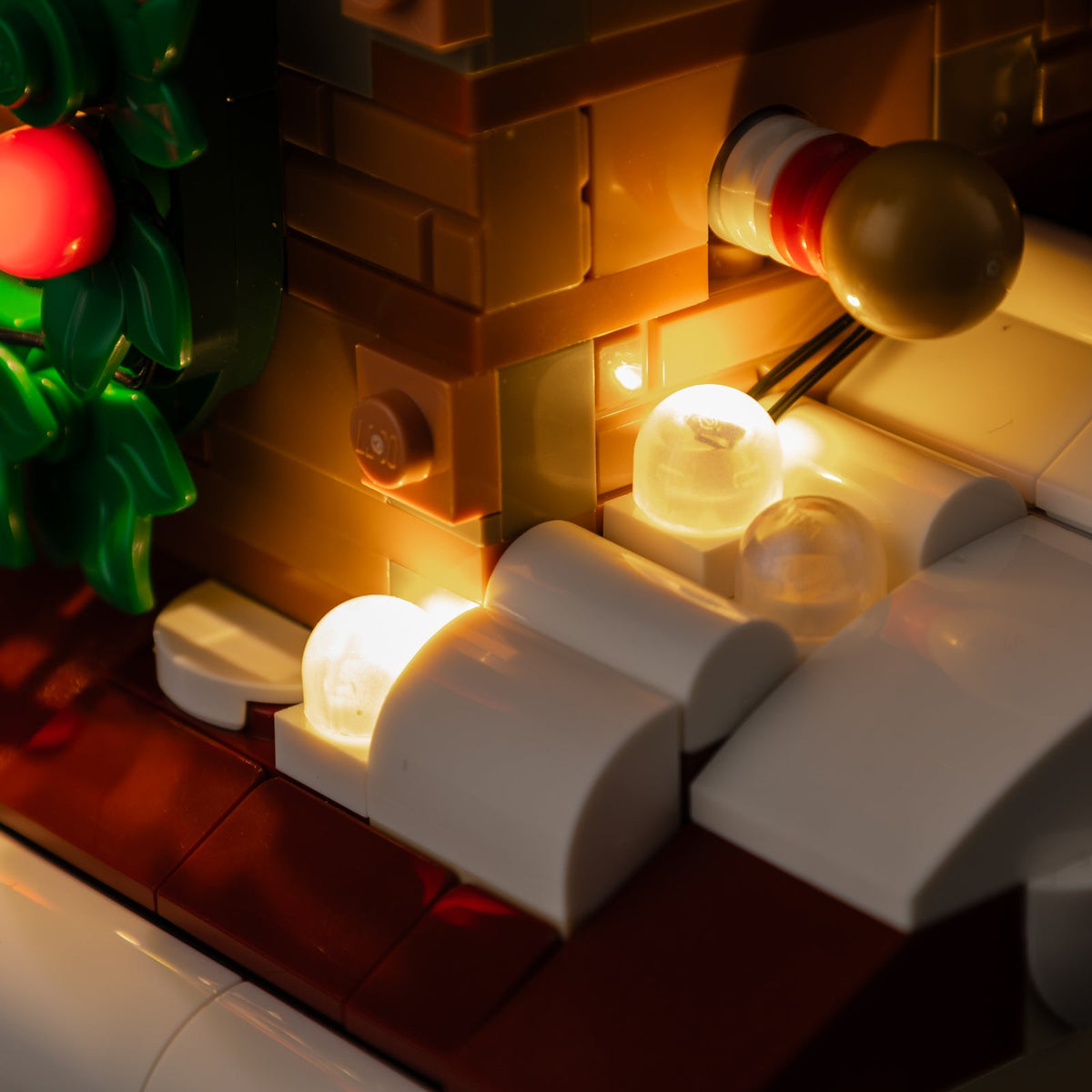 Close-up of the real chimney masonry, snow and warm dome lights beside the wreath in LEGO® Santa’s Holiday Countdown.